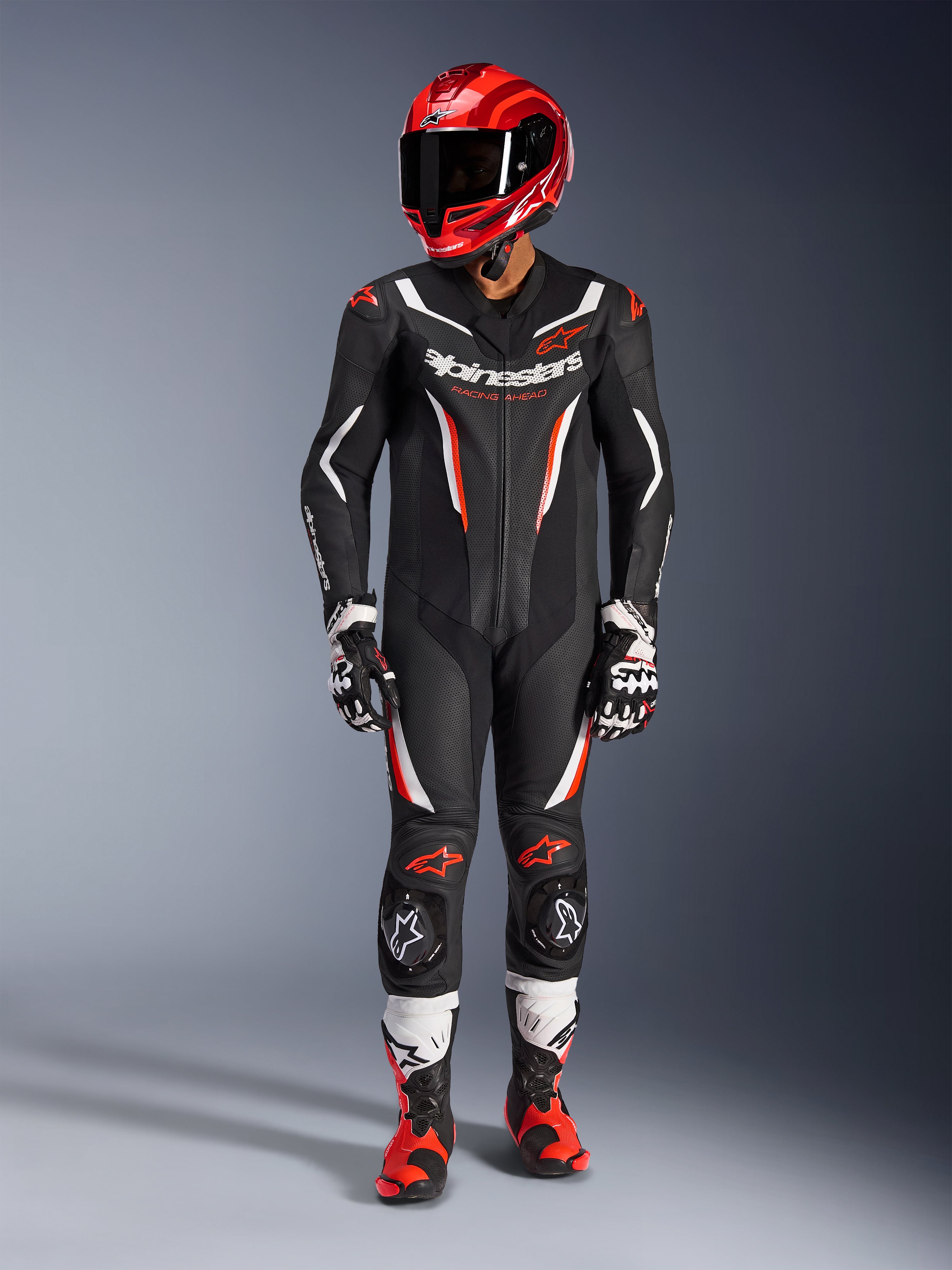 Fato de Pele Alpinestars GP Force V2 - 1 Peça, Preto, Branco e Vermelho Fluo, usado com um capacete de corrida vermelho, luvas pretas e brancas, e botas vermelhas e pretas, com painéis de pele perfurada e logótipos Alpinestars, equipamento profissional de corrida de motociclismo