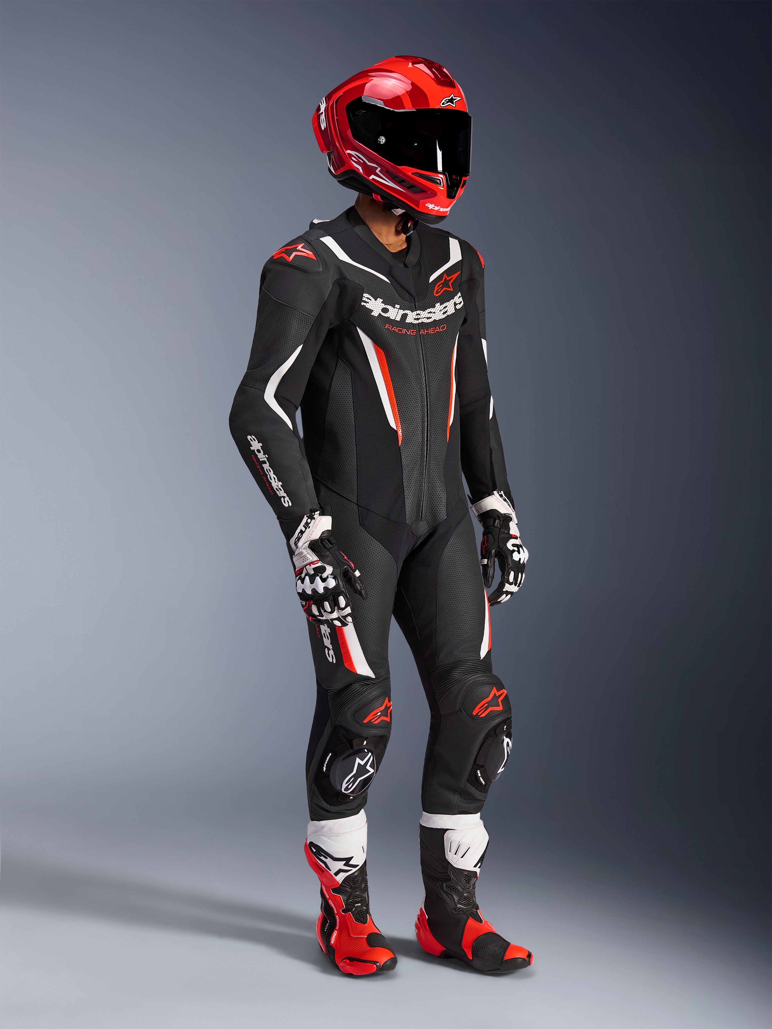 Fato de Cabedal Alpinestars GP Force V2 - 1 Peça, fato de corrida profissional em preto, branco e vermelho fluo, com painéis de pele perfurada e proteções DFS Lite. Equipamento de pista completo com capacete de corrida vermelho, luvas e botas a combinar.