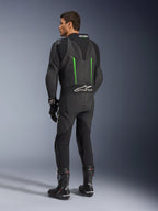 Alpinestars GP Force V2 Leather Suit, fato de motociclismo de 1 peça, preto com pormenores verdes, vista traseira mostrando a corcova aerodinâmica e o logótipo branco no painel de pele sanfonada, combinado com botas e luvas de corrida pretas.
