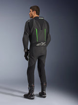 Alpinestars GP Force V2 Leather Suit, fato de motociclismo de 1 peça, preto com pormenores verdes, vista traseira mostrando a corcova aerodinâmica e o logótipo branco no painel de pele sanfonada, combinado com botas e luvas de corrida pretas.