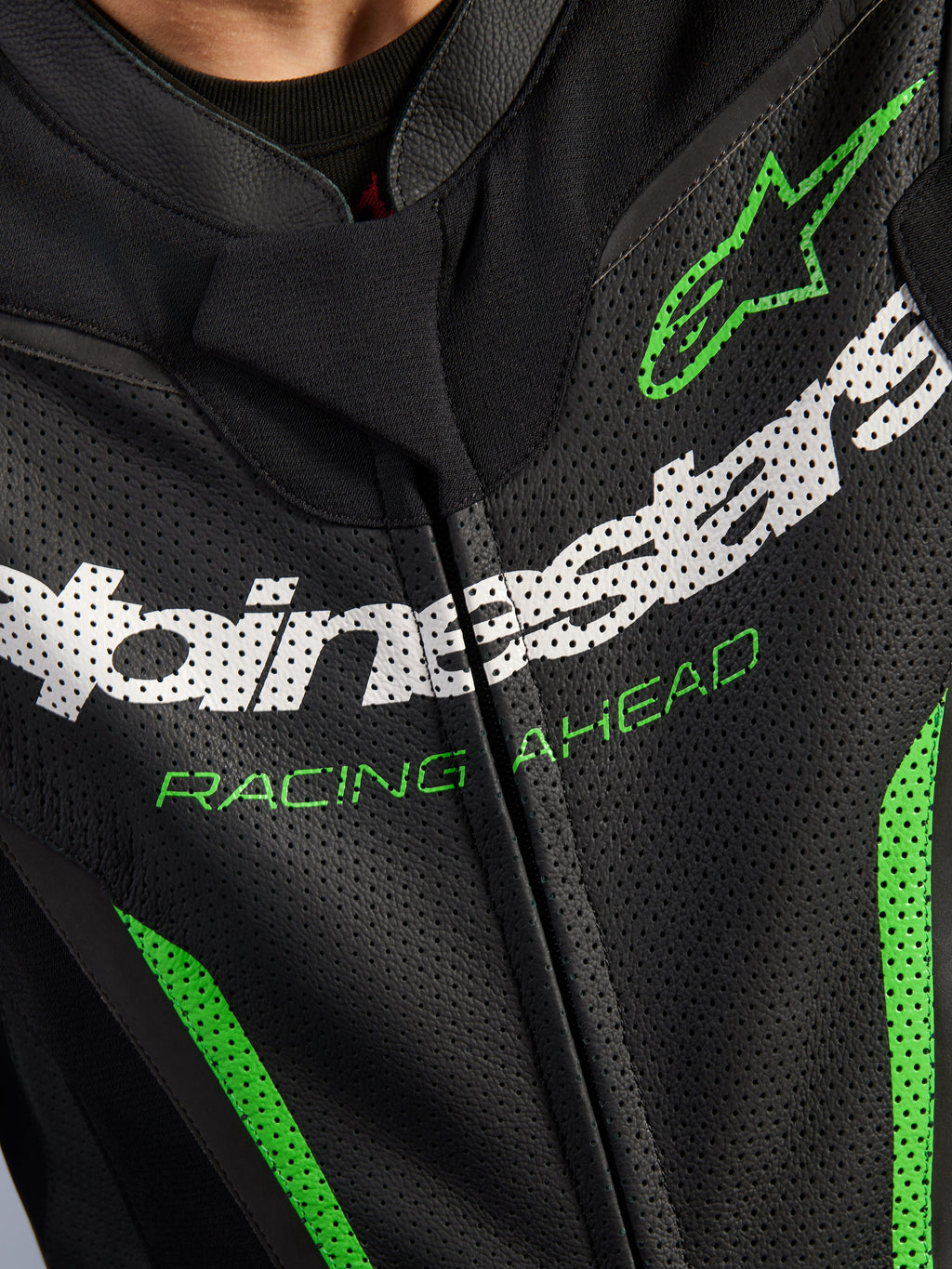 Alpinestars GP Force V2 Leather Suit - 1Piece, pormenor da zona do peito, pele perfurada preta com logótipo Alpinestars em branco, texto 'RACING AHEAD' em verde e detalhes em verde