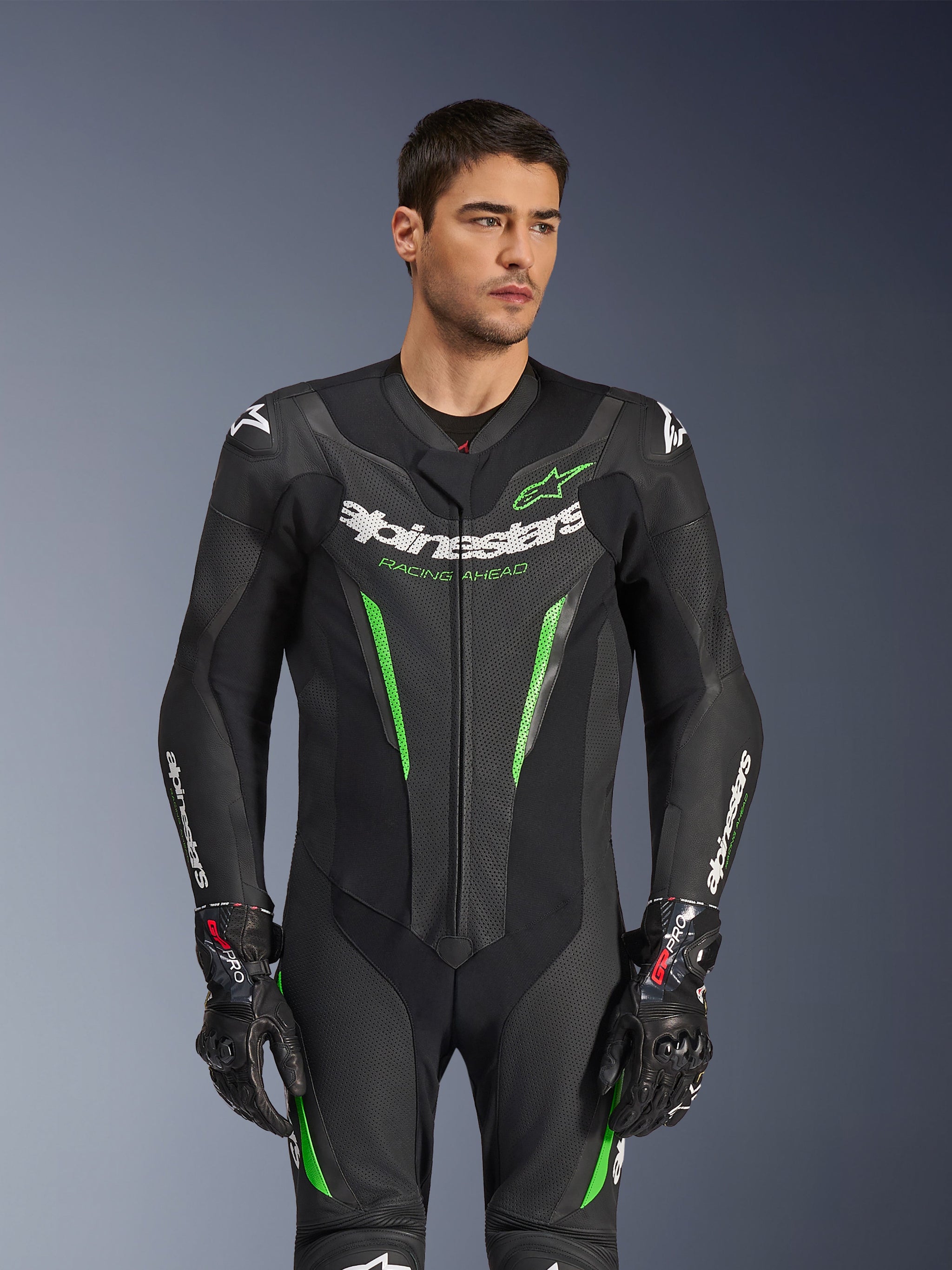 Alpinestars GP Force V2 Leather Suit - 1 Peça, fato de competição de motociclismo em preto e verde, vestido por modelo, apresentando painéis de pele perfurada, logótipo Alpinestars branco em destaque no peito e mangas, e proteção de ombros integrada para desempenho em pista.