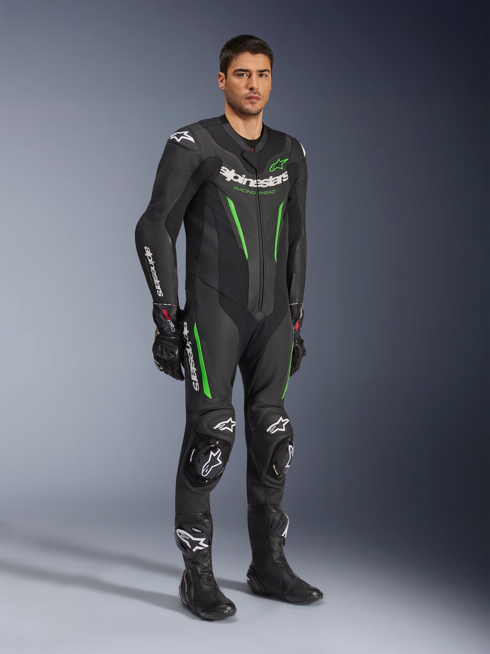 Alpinestars GP Force V2 Leather Suit 1-Piece, preto e verde, equipamento de corrida completo usado com luvas e botas pretas, com painéis de pele perfurada, logótipos Alpinestars brancos e deslizadores de joelho integrados, fato de performance profissional para pista