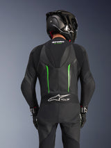 Vista traseira de um piloto com o Fato de Pele Alpinestars GP Force V2 em Preto e Verde, apresentando uma corcova aerodinâmica, o logótipo Tech-Air Ready no painel sanfonado na parte inferior das costas e construção em pele perfurada, acompanhado por um capacete de corrida em fibra de carbono preto.