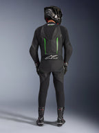 Piloto visto de trás a usar o fato de pele Alpinestars GP Force V2 - 1 Peça em preto e verde, combinado com um capacete de fibra de carbono preto, luvas de corrida pretas e botas pretas, apresentando uma corcova aerodinâmica e o logótipo Tech-Air Ready