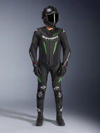 Piloto de motociclismo a usar o Fato de Pele Alpinestars GP Force V2 - 1 Peça em preto e verde, combinado com um capacete de fibra de carbono e luvas de corrida, com painéis de pele perfurada e logótipos Alpinestars brancos, equipamento profissional para pista e condução desportiva