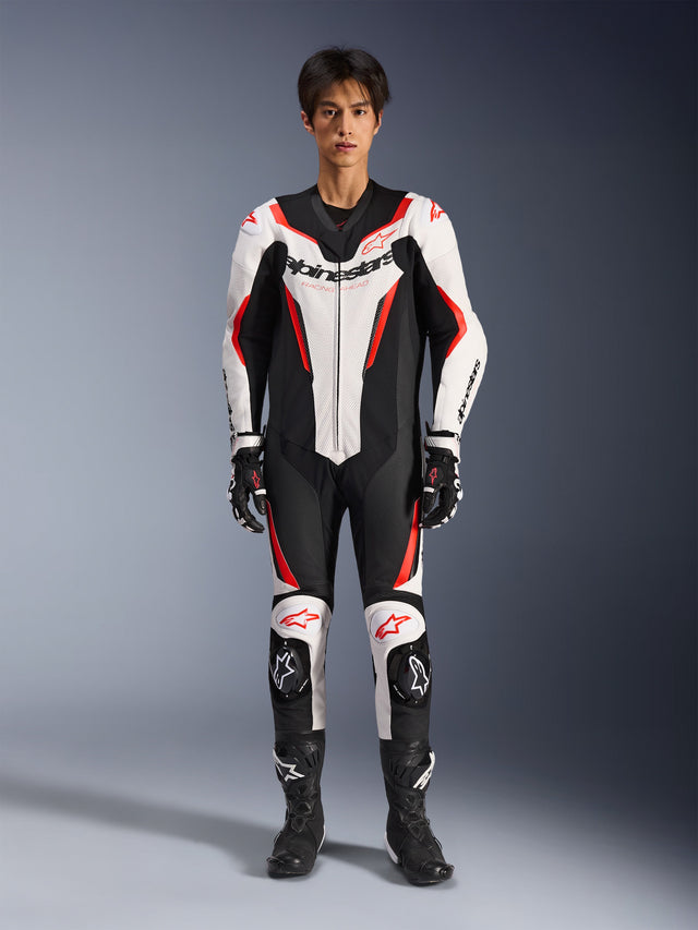 Alpinestars GP Force V2 Leather Suit - 1 Peça, Branco, Preto e Vermelho Fluo, fato de motociclismo de competição de uma peça em pele, vista frontal num modelo, com painéis perfurados e detalhes em vermelho, logótipo Alpinestars em destaque no peito, acompanhado por botas e luvas de competição profissionais