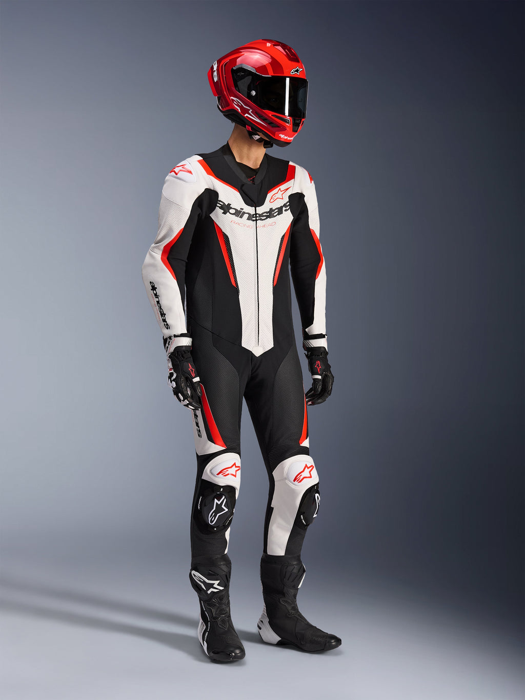Alpinestars GP Force V2 Leather Suit 1-Piece in White Black and Red Fluo, full-body studio shot of a rider wearing complete racing gear including a red helmet, black gloves, and black boots, featuring aerodynamic bovine leather construction with bold branding and integrated knee sliders.