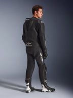 Modelo masculino a usar o Fato de Pele Alpinestars GP Force V2 de 2 Peças em preto com logótipos brancos, vista traseira de três quartos mostrando a corcova aerodinâmica e a marca Tech-Air Ready, combinado com botas e luvas de corrida pretas e brancas, equipamento profissional de motociclismo para desporto e pista.