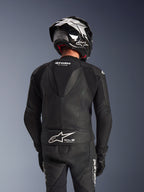 Fato de pele Alpinestars GP Force V2 de 2 peças, preto, vista traseira do piloto mostrando a corcova aerodinâmica, painéis de pele perfurada e zonas elásticas em acordeão nos ombros, com marca Tech-Air Ready na parte inferior das costas, usado com capacete de corrida e luvas a condizer.