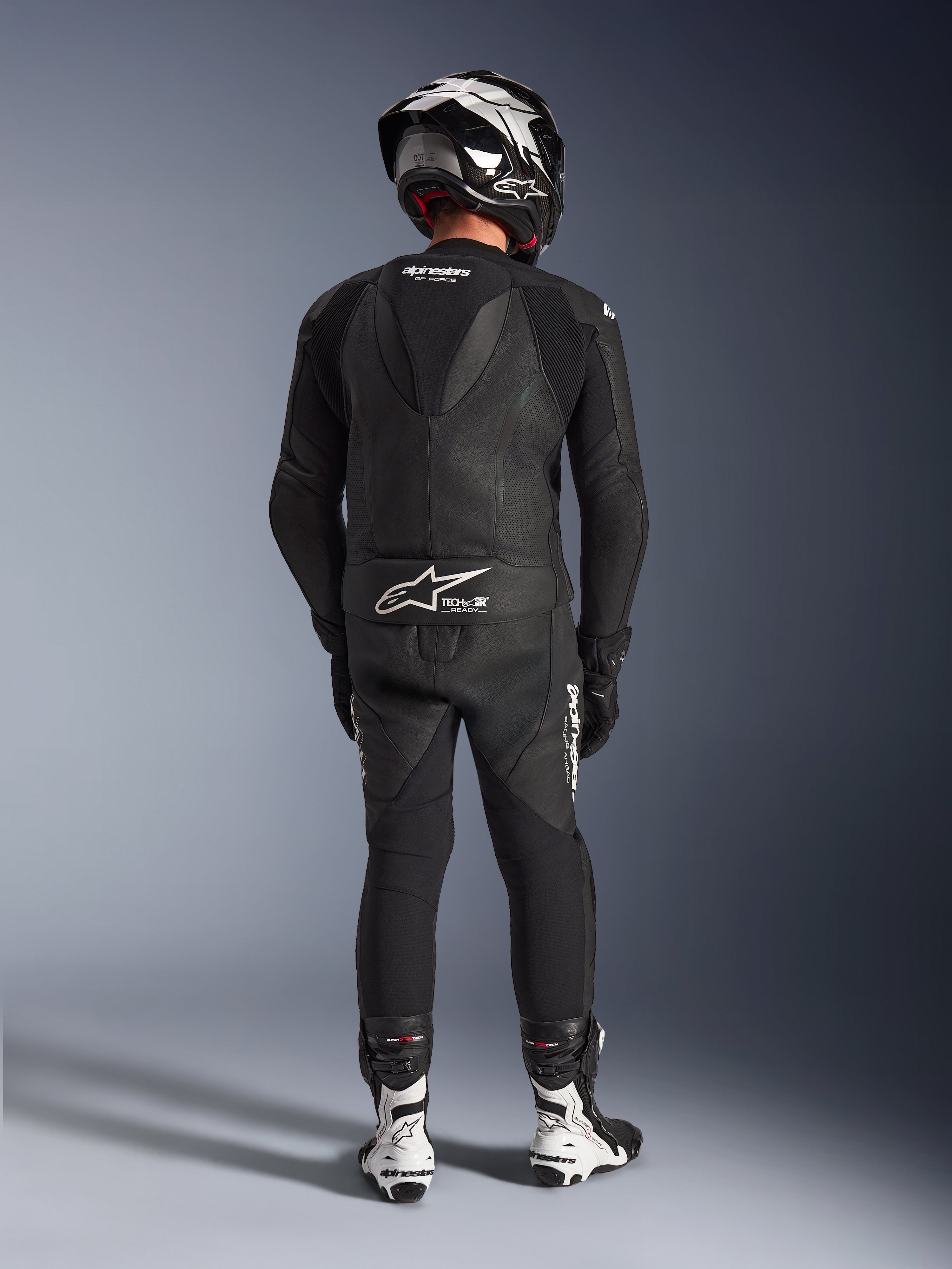 Fato de Cabedal Alpinestars GP Force V2 de 2 Peças em preto, vista traseira completa mostrando a corcova aerodinâmica e logótipo Tech-Air Ready, combinado com capacete preto e branco e botas de corrida brancas para performance profissional em pista
