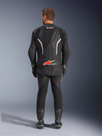 Vista traseira de um piloto a usar o Fato de Pele de 2 Peças Alpinestars GP Force V2, preto com detalhes em branco e vermelho, apresentando as marcas Alpinestars e Tech-Air Ready em destaque nas costas, complementado com luvas e botas de corrida pretas a condizer.