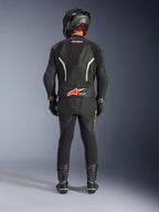 Motociclista visto de costas a usar o Fato de Pele Alpinestars GP Force V2 de 2 Peças, preto com detalhes em branco e vermelho fluo, apresentando uma corcova aerodinâmica e logótipo Tech-Air Ready, completo com capacete de corrida, luvas e botas pretos.