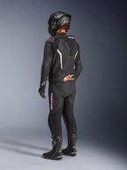 Alpinestars GP Force V2 Leather Suit - 2 Peças, fato de motociclismo em pele preto visto de costas, usado com capacete, luvas e botas pretas a combinar, com detalhes em branco e vermelho, bossa aerodinâmica com a marca Alpinestars, equipamento profissional de corrida e condução desportiva