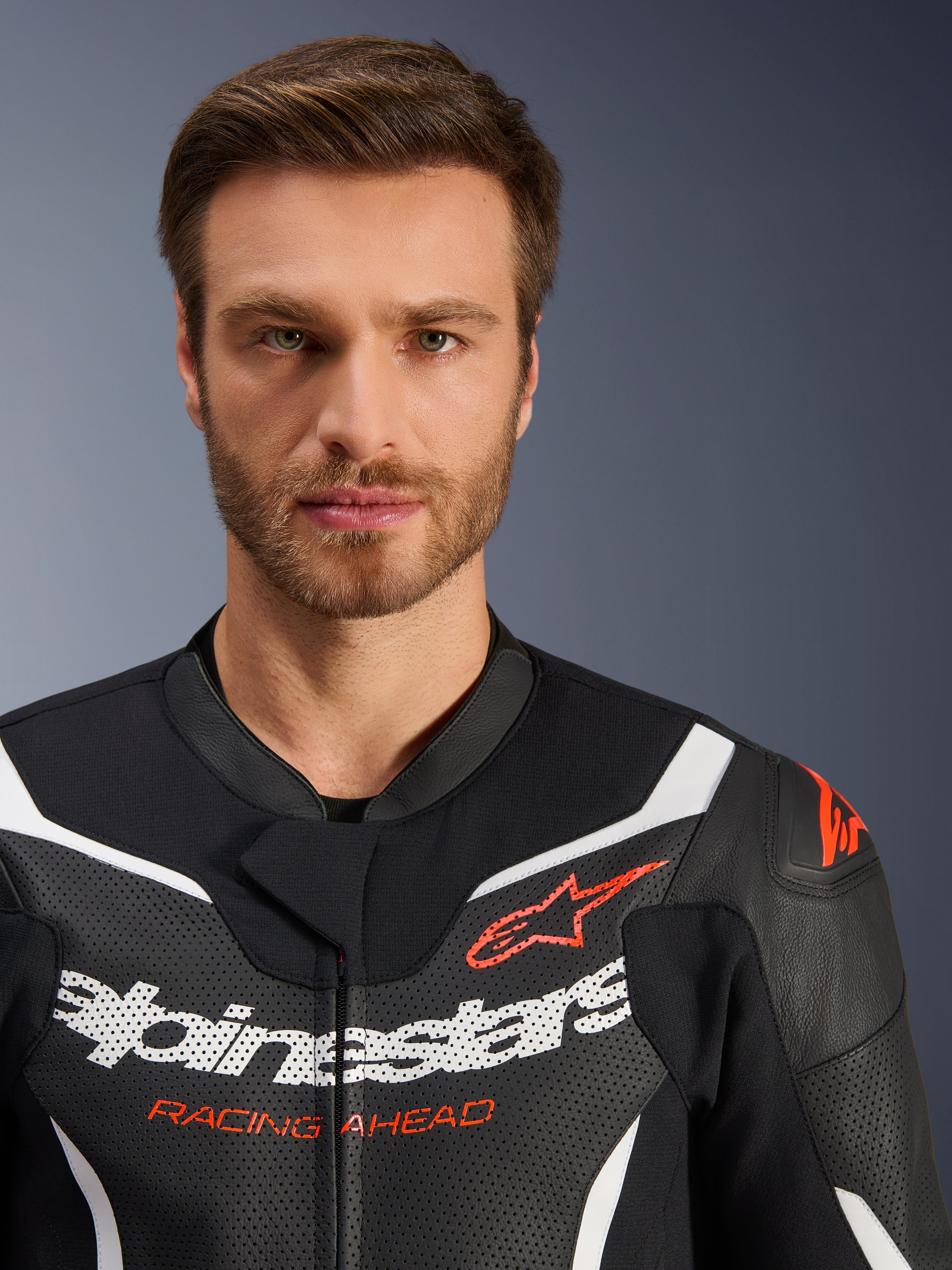 Casaco do fato de pele de 2 peças Alpinestars GP Force V2, preto, branco e vermelho fluo, retrato em grande plano com pele perfurada, logótipo Alpinestars a branco e texto 'RACING AHEAD' a vermelho, equipamento de motociclismo de alta performance
