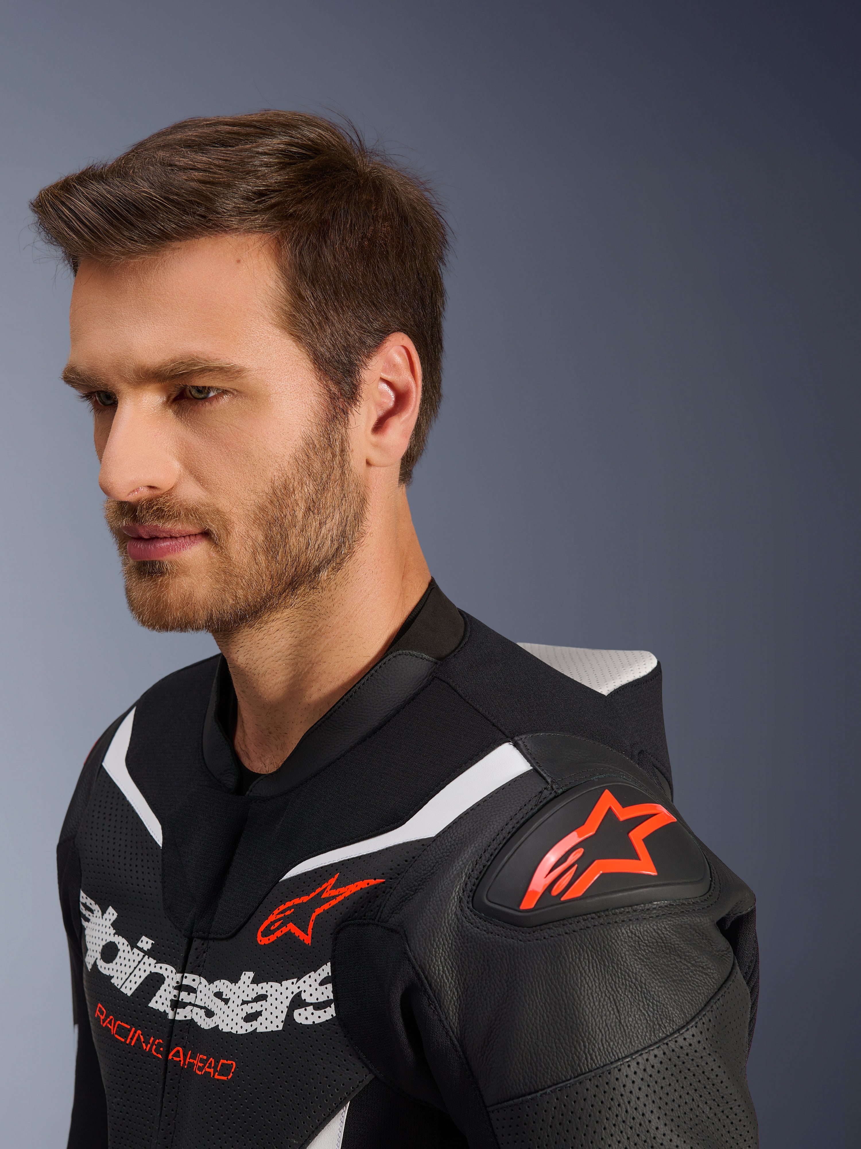 Fato de Pele Alpinestars GP Force V2 de 2 Peças, grande plano do casaco vestido por modelo masculino, preto, branco e vermelho fluo, com pele perfurada, logótipo de estrela vermelha no ombro, corcunda aerodinâmica e branding Alpinestars no peito, equipamento profissional de motociclismo de competição