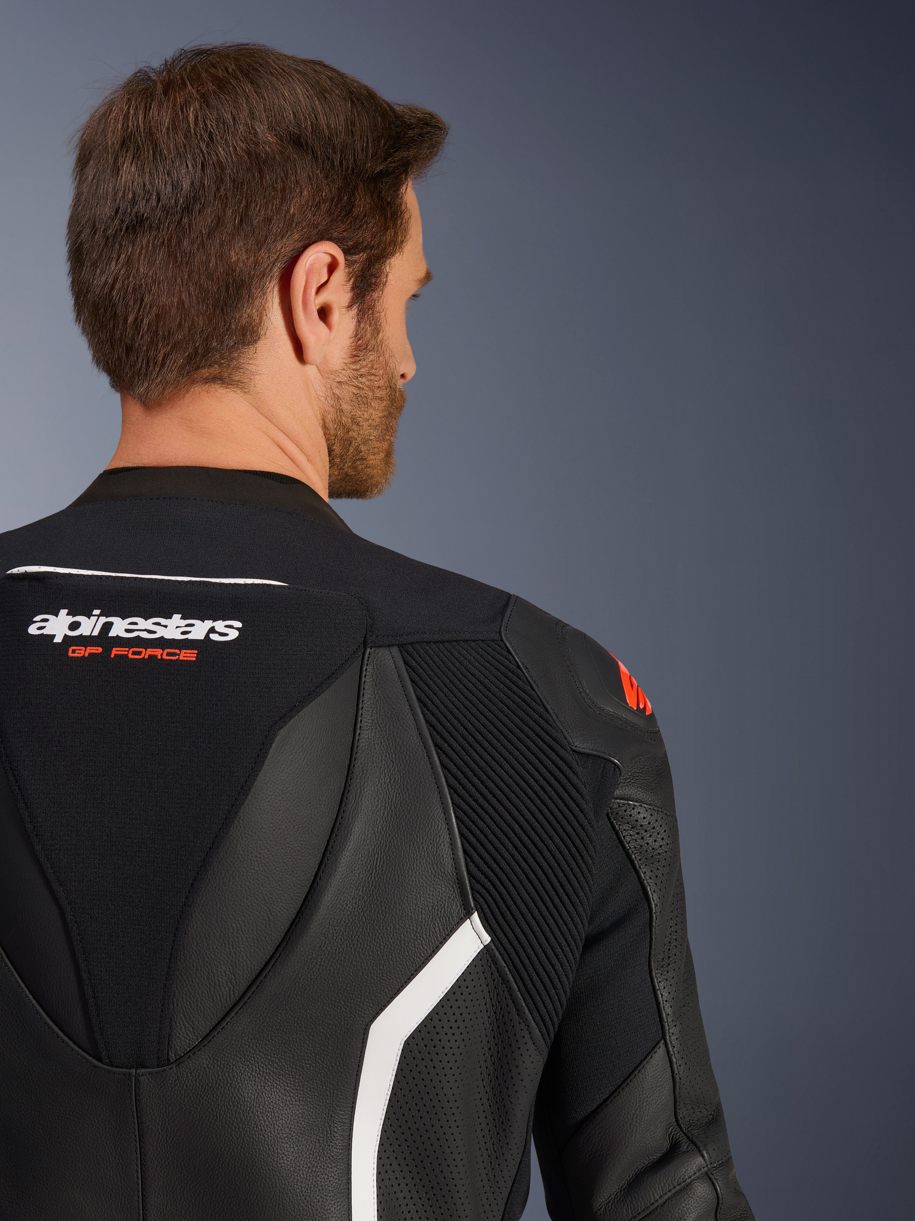 Fato de Pele GP Force V2 de 2 Peças, grande plano da parte superior das costas e do ombro num modelo masculino, em pele preta com pormenores em branco e vermelho, marca Alpinestars GP Force, realçando painéis perfurados e zonas elásticas em acordeão para competição.