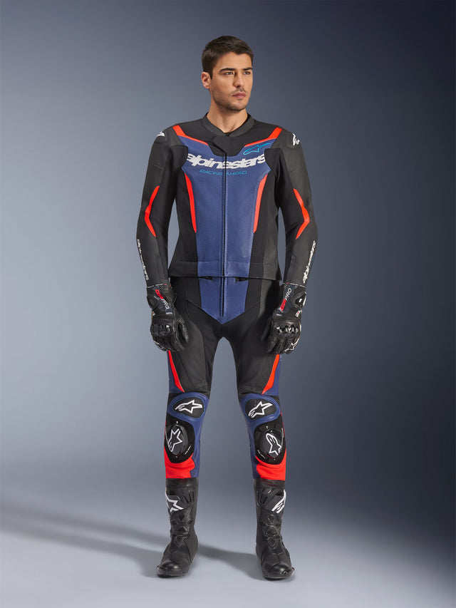Alpinestars GP Force V2 Leather Suit 2-Piece em preto, azul e vermelho fluorescente, com painéis azuis no peito e na parte inferior das pernas e detalhes em vermelho fluorescente vibrante, usado por um modelo masculino com botas e luvas de corrida pretas, vestuário de proteção profissional para desportos motorizados