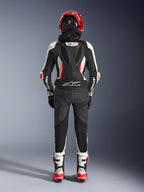 Woman Stella GP-R7 Leather Suit - 2Piece, rear view, Black White and Red Fluo, featuring aerodynamic hump with GP-R7 branding, Tech-Air Ready logo on the lower back, accordion stretch panels, and Alpinestars branding on the sleeves, worn with matching helmet and boots