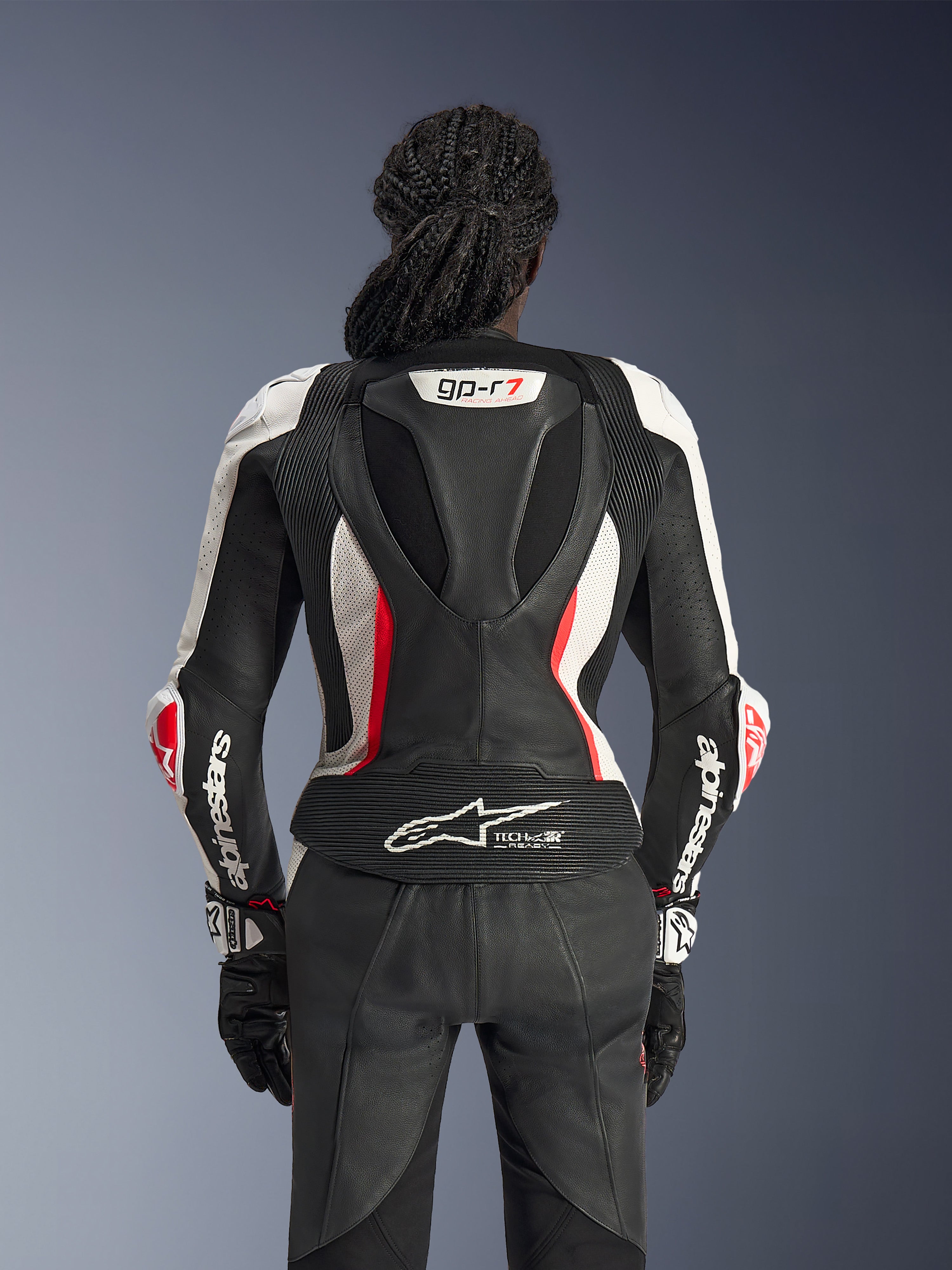Rear view of the Alpinestars Stella GP-R7 2-Piece Leather Suit in Black White and Red Fluo, featuring an aerodynamic race hump with GP-R7 branding, perforated leather panels, accordion stretch zones, and Tech-Air® Ready logo on the lower back.
