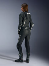 Fato de Cabedal de Uma Peça Alpinestars Stella GP-R7, preto, vista traseira no modelo mostrando a corcova aerodinâmica e o logótipo Alpinestars em branco nas mangas e pernas, usado com botas de corrida pretas, equipamento de motociclismo de alta performance