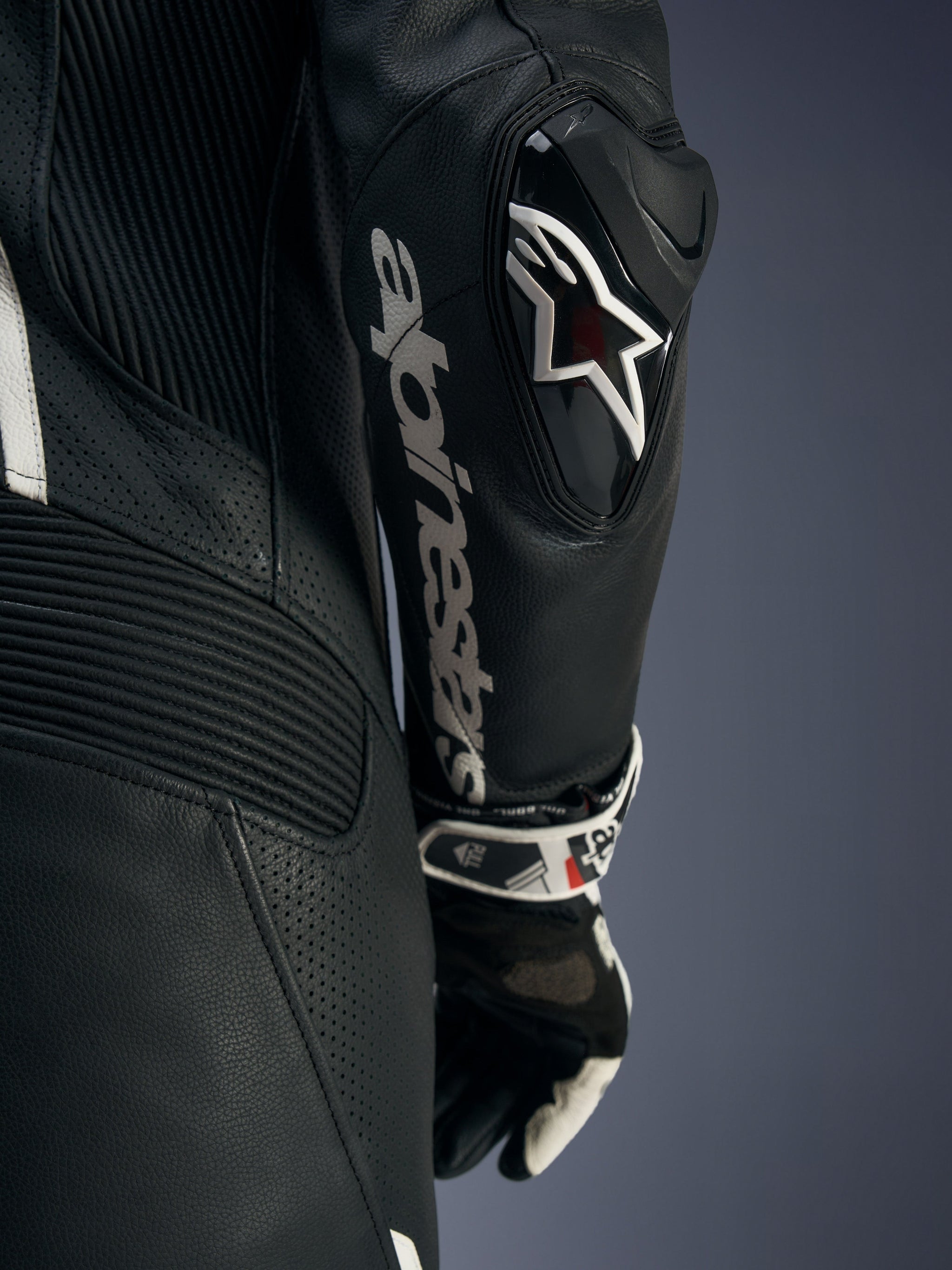 Fato de Cabedal de 1 Peça Alpinestars Stella GP-R7, preto, grande plano do braço com o deslizador de cotovelo DFS RR com o logótipo Astars, texto Alpinestars em branco no antebraço e zonas de cabedal perfurado