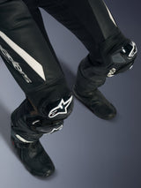 Fato de Cabedal de Uma Peça Alpinestars Stella GP-R7, Preto, vista aproximada das pernas e joelhos com logótipos brancos, sanfonas de couro elástico e deslizadores de joelho GP DFS RR, usado com botas de corrida de motociclismo pretas.