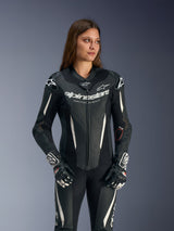 Alpinestars Stella GP-R7 Leather Suit, fato de corrida de uma peça para mulher, preto com detalhes em branco e cinzento, vestido por uma modelo, com construção em couro perfurado e logótipo Alpinestars no peito, equipamento de motociclismo de alta performance