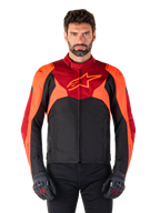 Alpinestars T-Jaws V4 Waterproof Jacket, casaco de motociclismo têxtil desportivo, preto com pormenores em vermelho fluo e vermelho escuro, usado por um modelo masculino com luvas a condizer, equipamento técnico de condução com logótipo de estrela proeminente no peito.
