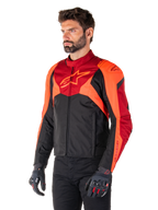 Casaco Impermeável Alpinestars T-Jaws V4, Preto, Vermelho Fluo e Vermelho Escuro, vestido por um modelo masculino com calças pretas e luvas de motociclismo, silhueta desportiva agressiva com o logótipo Alpinestars no peito, vista de três quartos