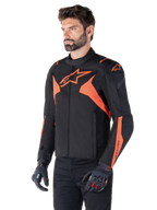 Alpinestars T-Jaws V4 Waterproof Jacket, preto e vermelho fluo, casaco desportivo de motociclismo vestido por um modelo masculino, com logótipos de estrela cor de laranja destacados no peito e nos ombros, combinado com luvas e calças pretas