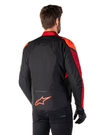 Vista traseira de um homem a usar o Casaco Impermeável Alpinestars T-Jaws V4 em preto, vermelho fluo e vermelho escuro, com pormenores em vermelho vibrante nos ombros e mangas, um logótipo Alpinestars em vermelho fluo na parte inferior das costas, combinado com calças e luvas pretas.
