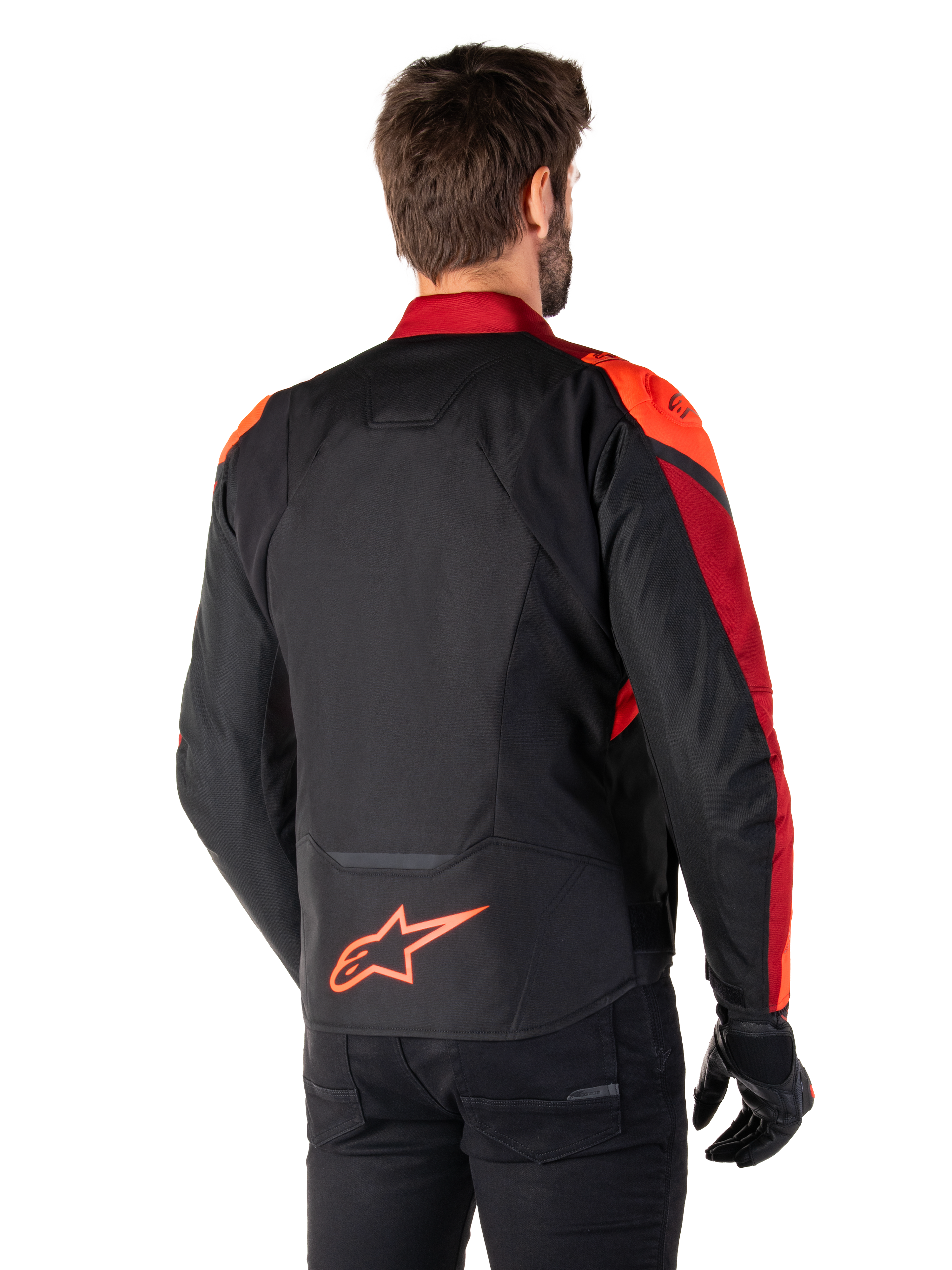 Vista traseira de um homem a usar o Casaco Impermeável Alpinestars T-Jaws V4 em preto, vermelho fluo e vermelho escuro, com pormenores em vermelho vibrante nos ombros e mangas, um logótipo Alpinestars em vermelho fluo na parte inferior das costas, combinado com calças e luvas pretas.