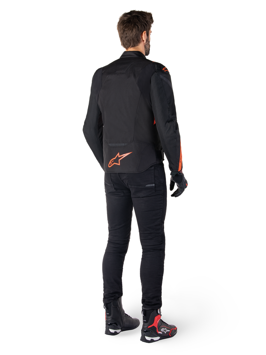 Casaco Impermeável Alpinestars T-Jaws V4, preto e vermelho fluo, vista traseira usado por um piloto masculino, com logótipo vermelho fluo vibrante nas costas, calças de condução pretas e botas técnicas, vestuário de motociclismo desportivo.