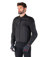 Male rider wearing the Alpinestars T-Jaws V4 Waterproof Jacket in Black Black, paired with black pants and protective gloves, featuring a sleek sport fit, tonal Alpinestars logos on the chest and shoulders, and a high-performance textile construction.