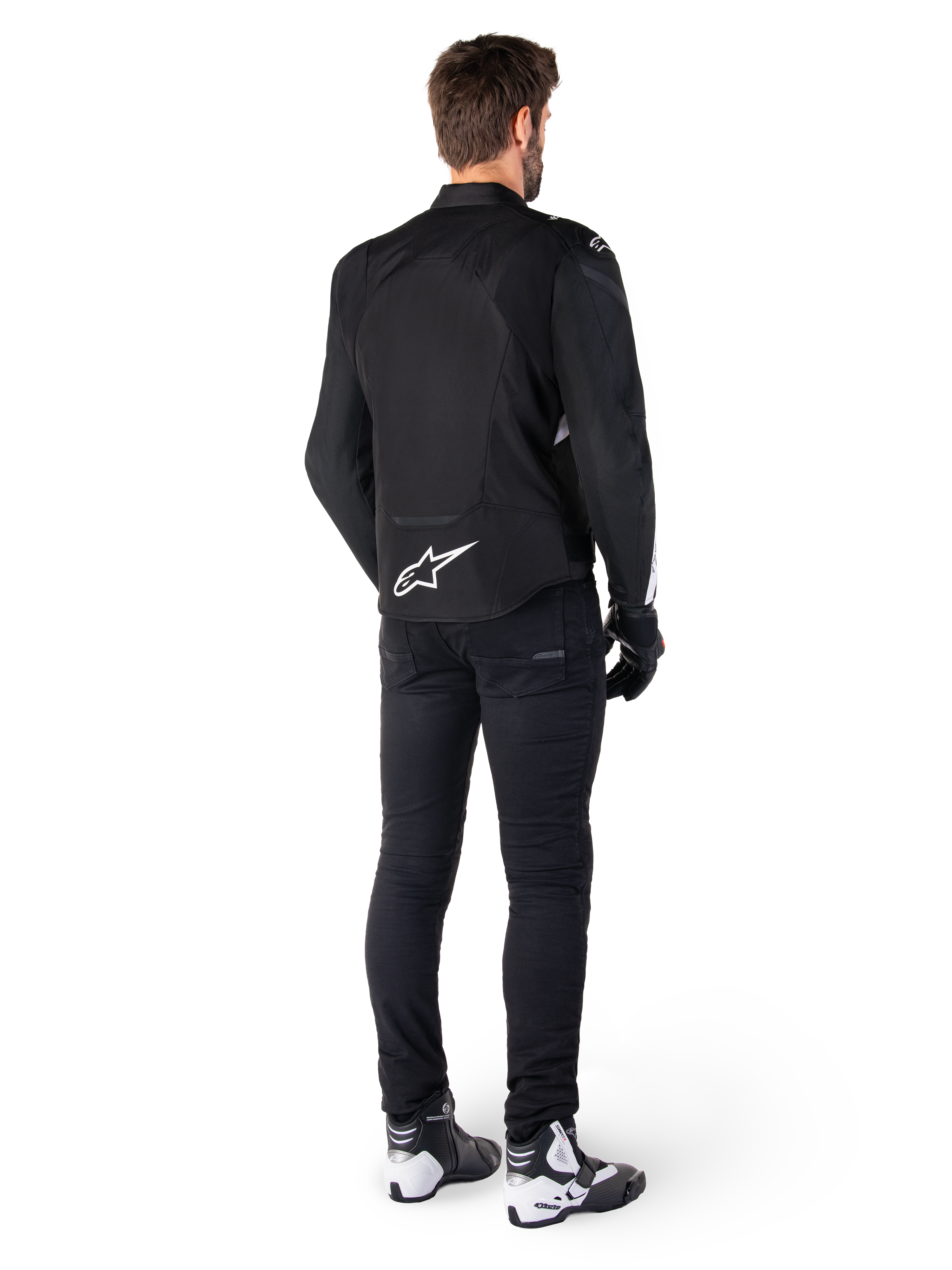 Alpinestars T-Jaws V4 Waterproof Jacket, Black and White, rear view showing white star logo on lower back, worn by model with black riding pants, black gloves, and white and black motorcycle boots.