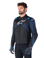 Casaco Impermeável Alpinestars T-Jaws V4, casaco de motociclismo, preto, azul escuro e azul Blithe, usado por um modelo com luvas a combinar e calças pretas, com logótipos Alpinestars brancos no peito e ombros e detalhes azuis nas mangas, equipamento têxtil desportivo