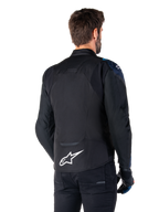 Casaco Impermeável Alpinestars T-Jaws V4, vista traseira, preto com detalhes em azul escuro e azul Blithe, logótipo de estrela branca na parte inferior das costas, silhueta desportiva, usado com calças pretas e luvas de motociclismo