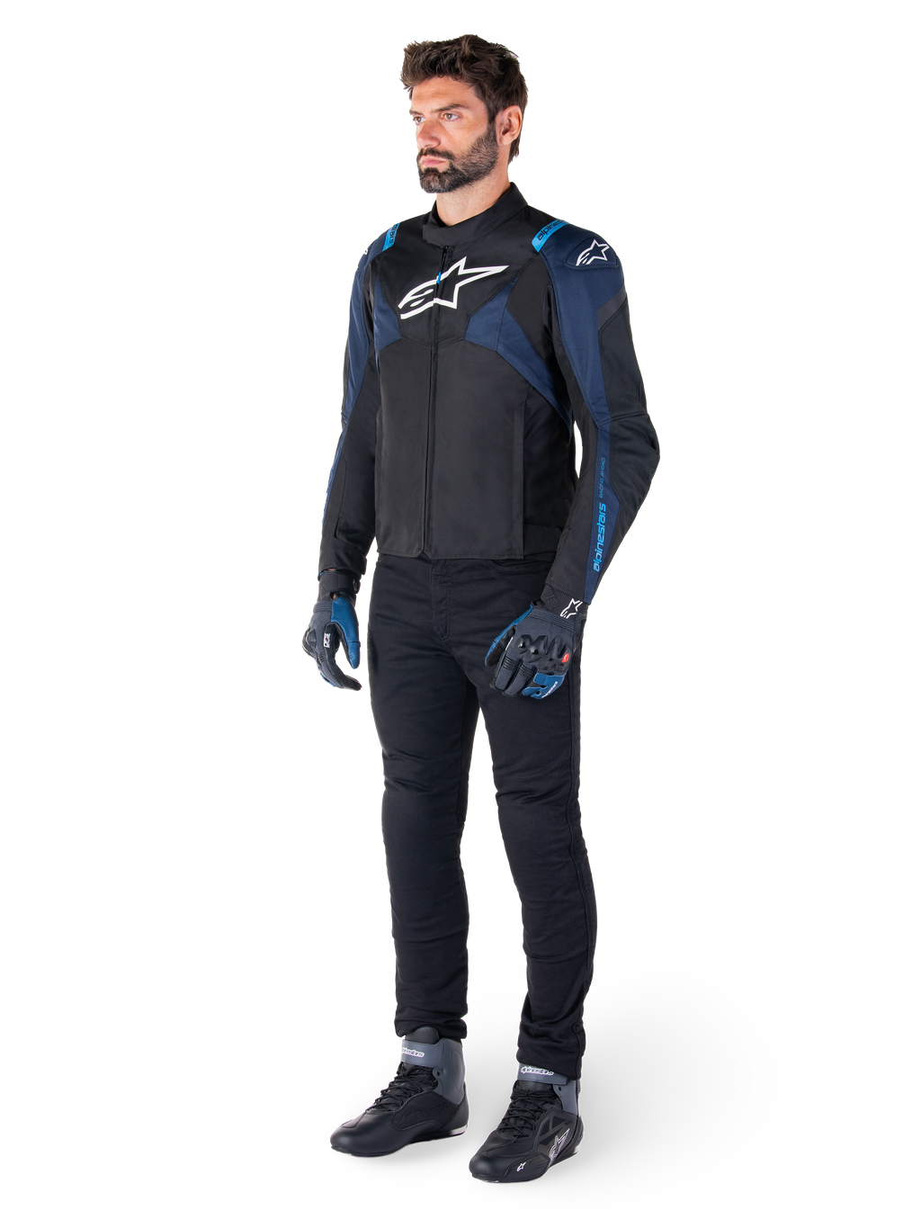 Casaco Impermeável Alpinestars T-Jaws V4 em preto, azul escuro e azul Blithe, vestido por um modelo com calças de motociclismo pretas e botas de condução, com logótipo Alpinestars branco no peito e detalhes azuis nos ombros, equipamento de condução com ajuste desportivo