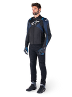Casaco Impermeável Alpinestars T-Jaws V4 em preto, azul escuro e azul Blithe, vestido por um modelo com calças de motociclismo pretas e botas de condução, com logótipo Alpinestars branco no peito e detalhes azuis nos ombros, equipamento de condução com ajuste desportivo