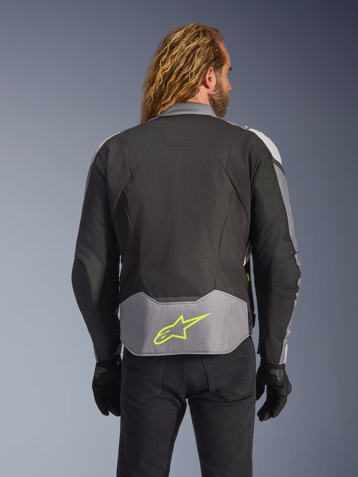 Alpinestars T-Jaws V4 Waterproof Jacket, Black Ice Gray Dark Gray, rear view on model, featuring a light gray lower back panel with a prominent neon yellow star logo, multi-panel textile construction, and a sporty silhouette, worn with black gloves and dark pants.
