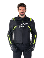 Casaco Impermeável Alpinestars T-SPS V2, casaco de motociclismo, preto com detalhes em branco e amarelo fluorescente, usado por um modelo com luvas pretas, com um logótipo de estrela branco no peito e riscas amarelo néon nas mangas e ombros, equipamento têxtil de estilo desportivo para todas as condições meteorológicas