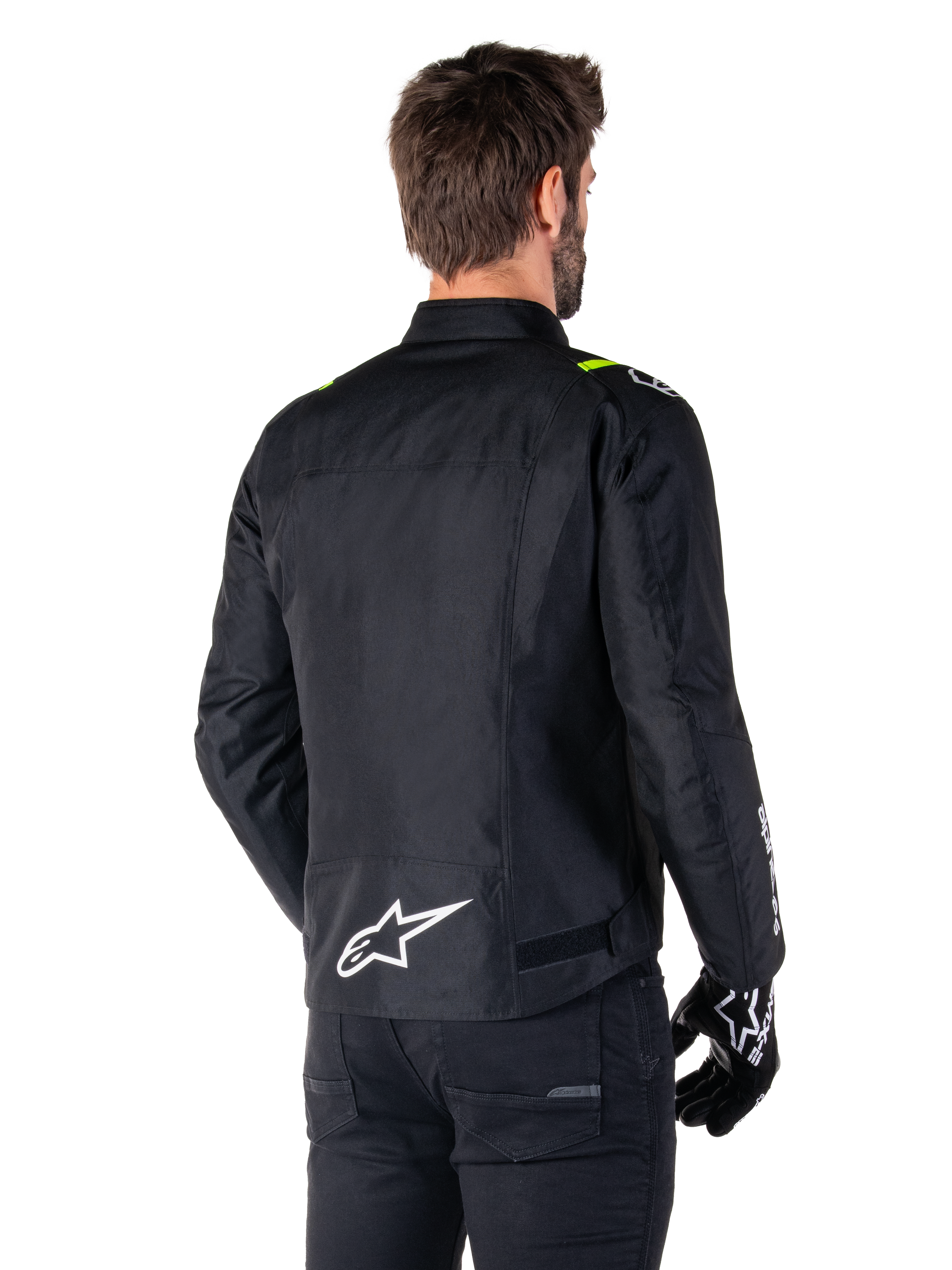 Alpinestars T-SPS V2 Waterproof Jacket, Preto Branco Amarelo Fluo, vista traseira de modelo masculino a usar o casaco de motociclismo têxtil, com logótipo branco na parte inferior das costas e detalhes em amarelo fluo nos ombros, combinado com calças e luvas pretas.