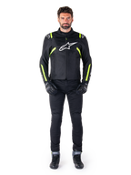 Casaco Alpinestars T-SPS V2 Waterproof, Preto, Branco e Amarelo Fluo, usado por um modelo com calças e luvas de condução pretas, com o logótipo Alpinestars branco no peito e detalhes fluorescentes nos ombros e mangas, equipamento de motociclismo de corte desportivo