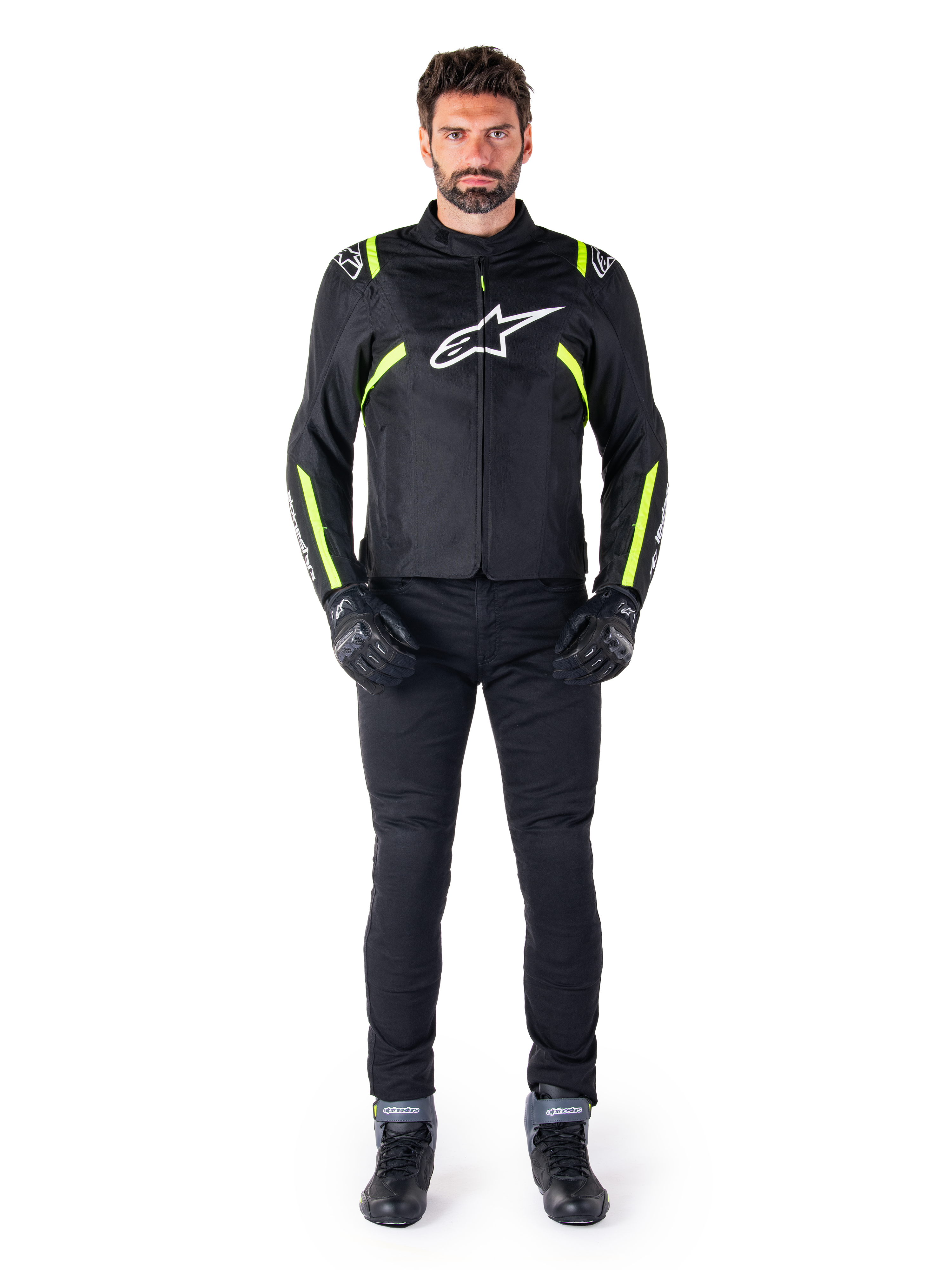 Casaco Alpinestars T-SPS V2 Waterproof, Preto, Branco e Amarelo Fluo, usado por um modelo com calças e luvas de condução pretas, com o logótipo Alpinestars branco no peito e detalhes fluorescentes nos ombros e mangas, equipamento de motociclismo de corte desportivo