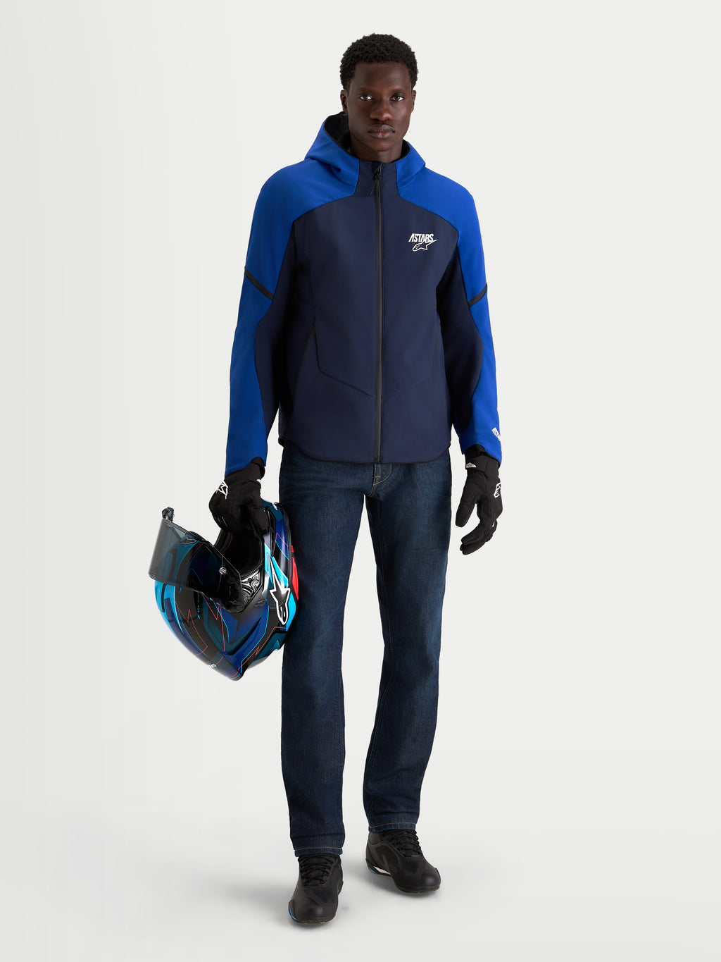 Alpinestars Aeroshell Waterproof Jacket, Men's Night Navy and Bright Blue motorcycle sports softshell jacket with an open-slot hood and CE certification, worn by a model holding a matching helmet