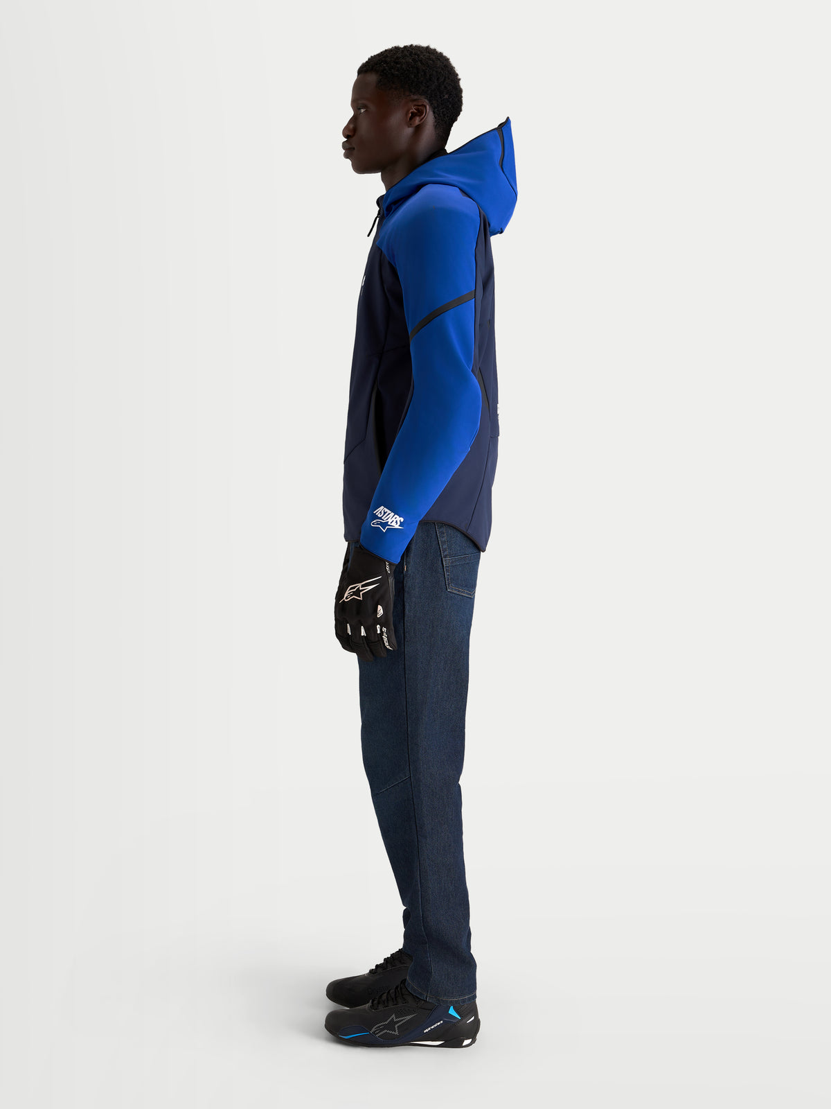 Alpinestars Aeroshell Waterproof Jacket, men's motorcycle riding jacket in night navy and bright blue, featuring an open-slot hood and adaptive stretch softshell construction, worn by a model in profile view