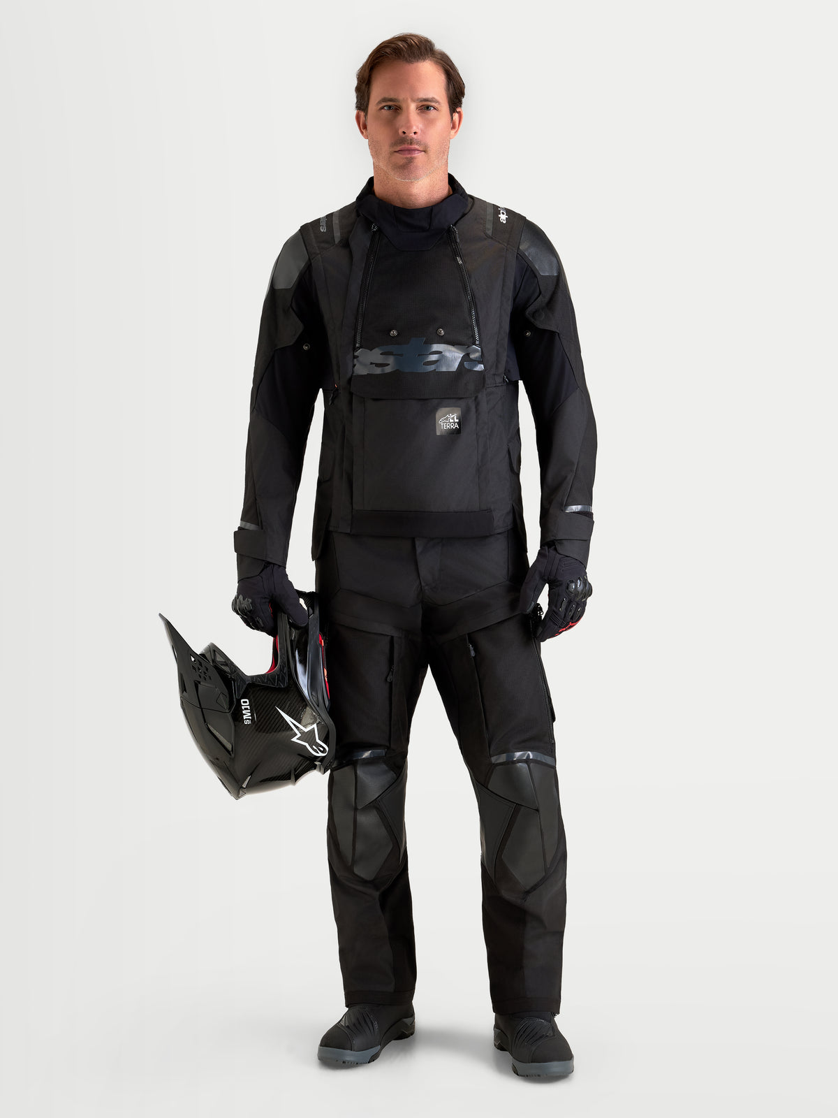 Alpinestars Harok V2 Drystar gear set, casaco e calças de moto para aventura para homem, pretos, num modelo a segurar um capacete a condizer, vestuário de condução impermeável para todas as condições meteorológicas