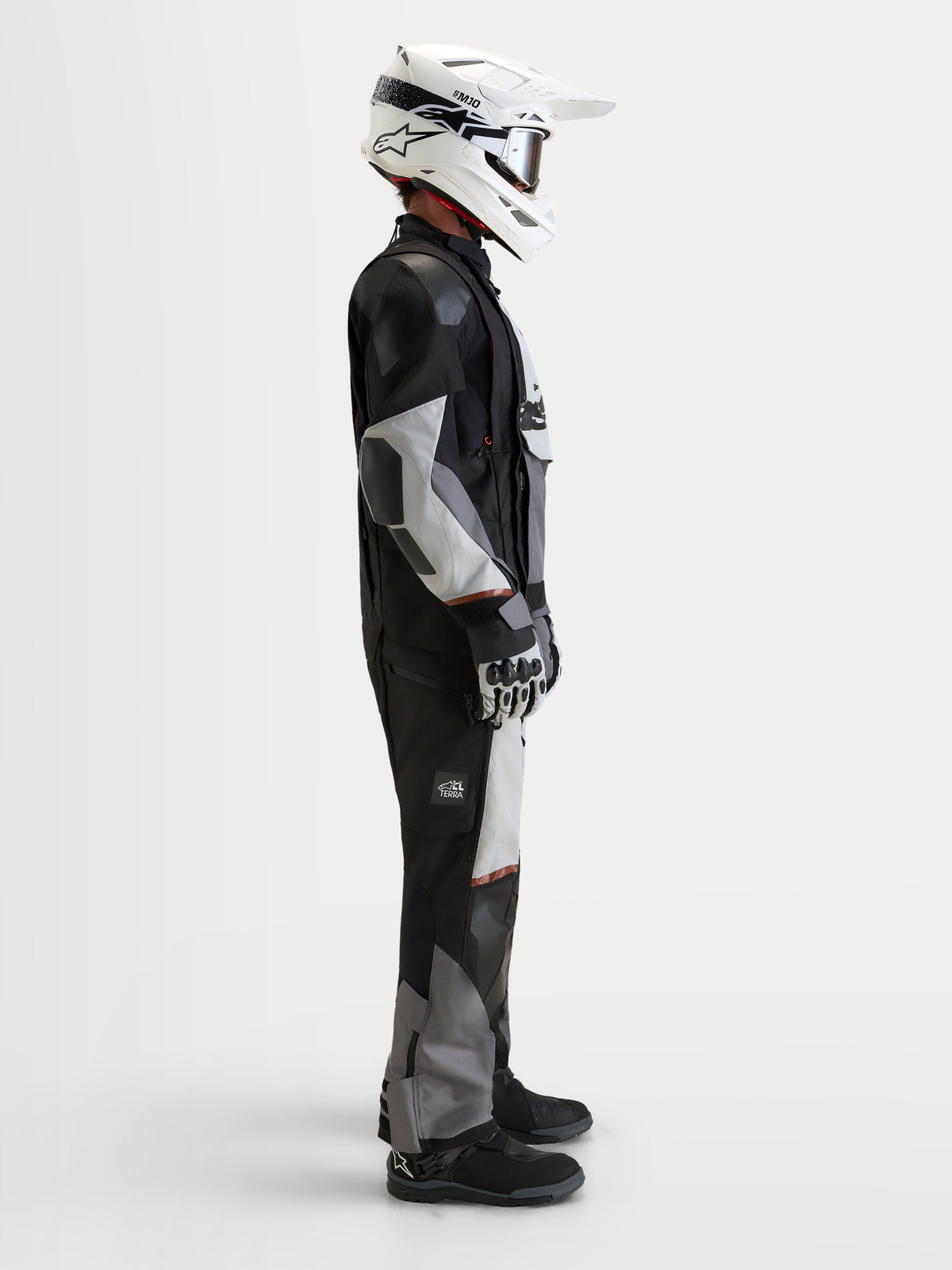 Alpinestars Harok V2 Drystar casaco, casaco de moto all-terrain de aventura para homem, cinzento-escuro, cinzento-gelo e preto, num modelo com capacete branco e equipamento de aventura em vista lateral de estúdio