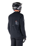 Vista traseira de um motociclista a usar o Casaco Alpinestars AMT-8 Stretch Drystar® XF em preto, com a marca 'AMT Alpinestars Motion Technology' nas costas, ventilação técnica com fecho de correr, combinado com um capacete e luvas de motociclismo pretos.